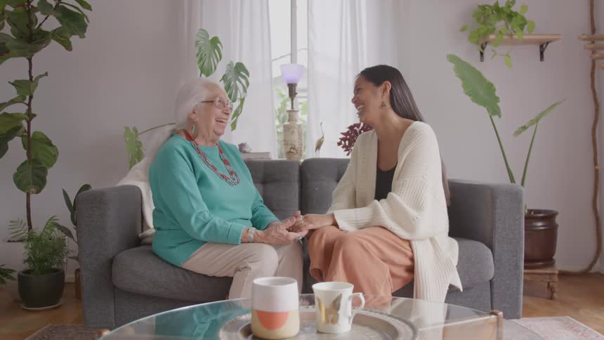 Two women hold hands and laugh on the couch