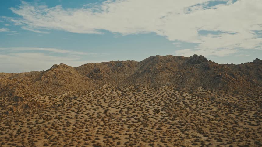 Arid mountain range covered with sparse vegetation under a partly cloudy sky