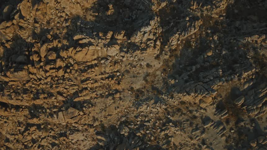 A top down aerial shot slowly drifts over a rugged rocky landscape bathed in warm golden light