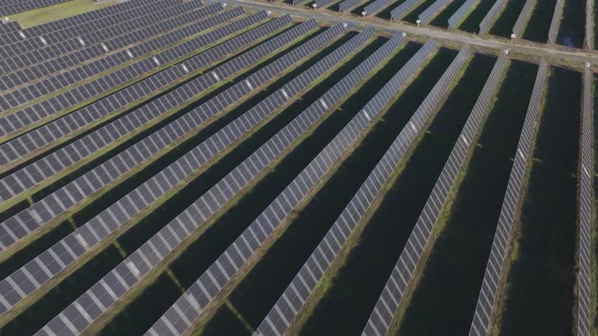 Aerial view of a vast solar farm with rows of panels across a field