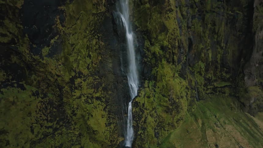 Waterfall flows down a mosscovered cliff amid rocky formations