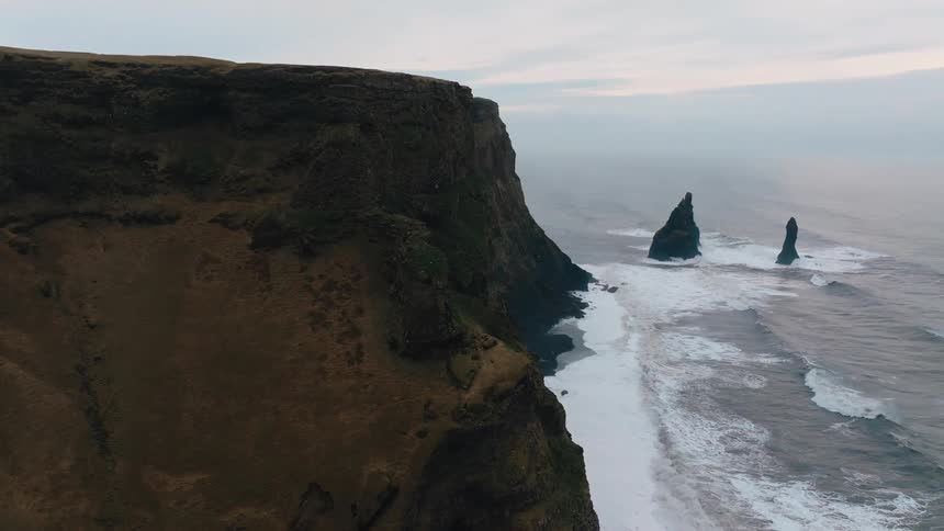 Seaside cliffs with waves crashing and rock formations in the distance