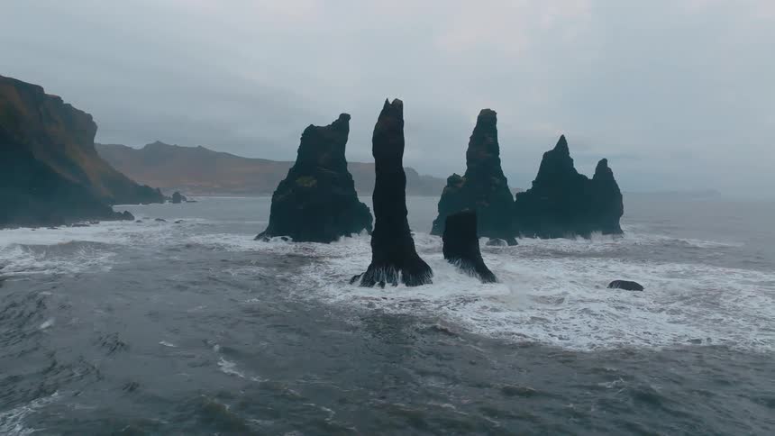 Jagged rock formations rise from rough sea beneath cloudy sky in dramatic coastal setting