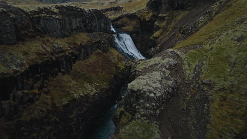 Waterfall flows between dark rock formations in a mosscovered valley