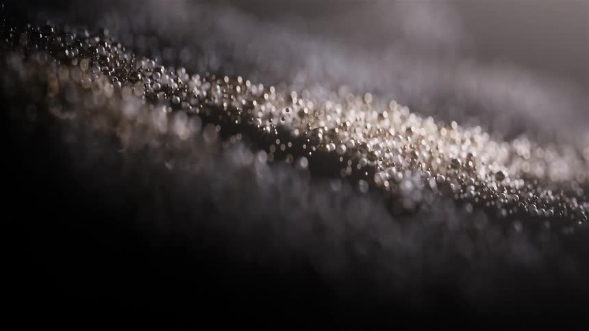Illuminated grains of sand form a shimmering line on a dark surface