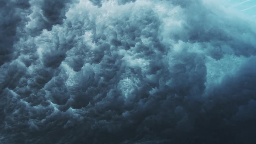 A wave crest descends forming a mass of bubbles air and foam creating underwater turbulence
