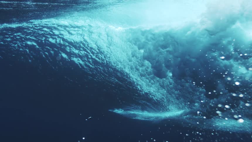 Ocean wave builds with force beneath the surface revealing turbulent motion and shades of blue