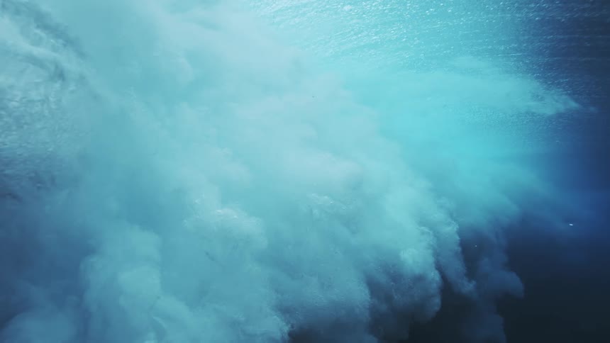 Foam moves around underwater as the wave crashes