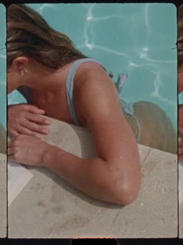 Woman in a bikini leans on the pool edge while reading a book