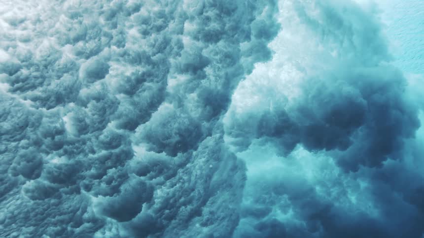 Ocean waves form and crash violently into the water at midday churning up a surge of bubbles and foam as sunlight glints off the restless surface