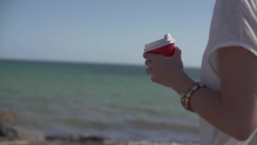 Woman holding a cup walking by the water