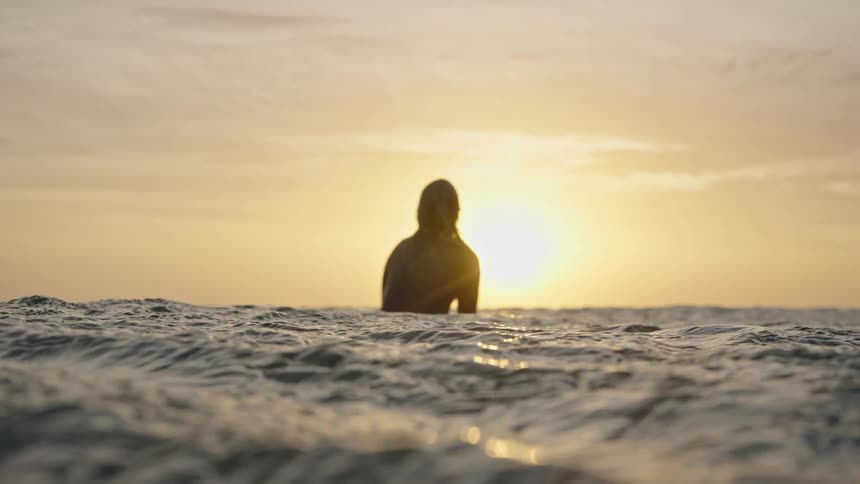 Surfer watching the sunset while sitting on the board in the sea