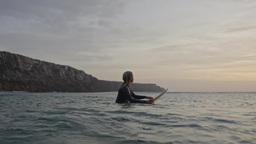 The woman looks up at the cloudy sky on her surfboard
