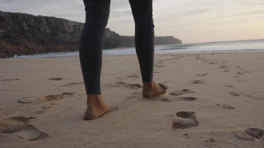 The woman is walking towards the water with her surfboard