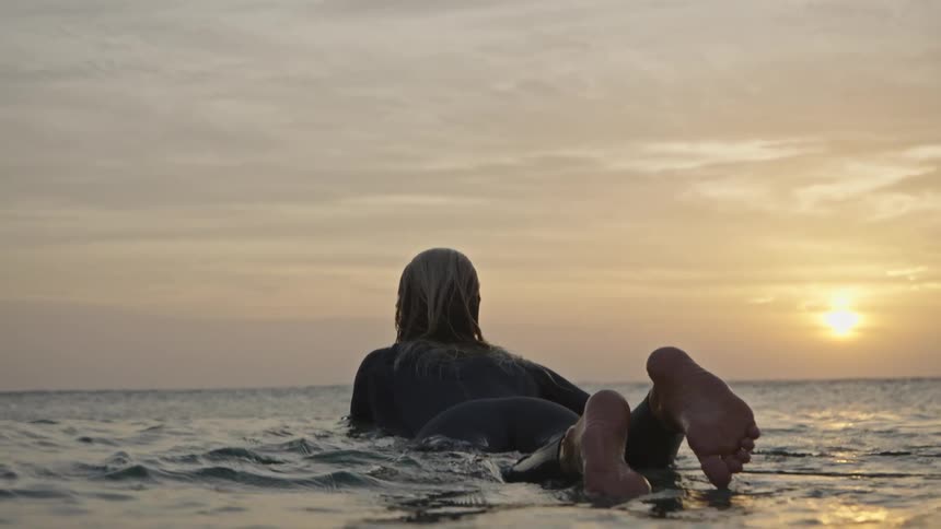 The woman floats on her surfboard watching the sun rise
