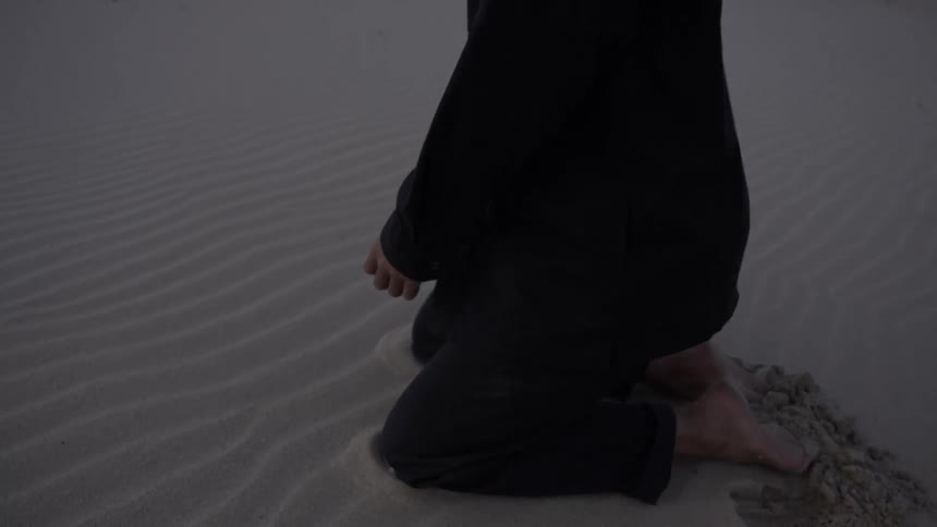 The woman kneels and picks up a handful of sand