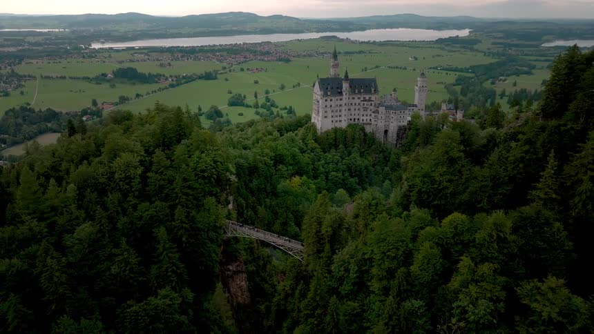 Aerial view of a castle on a wooded hill overlooking a valley and lake