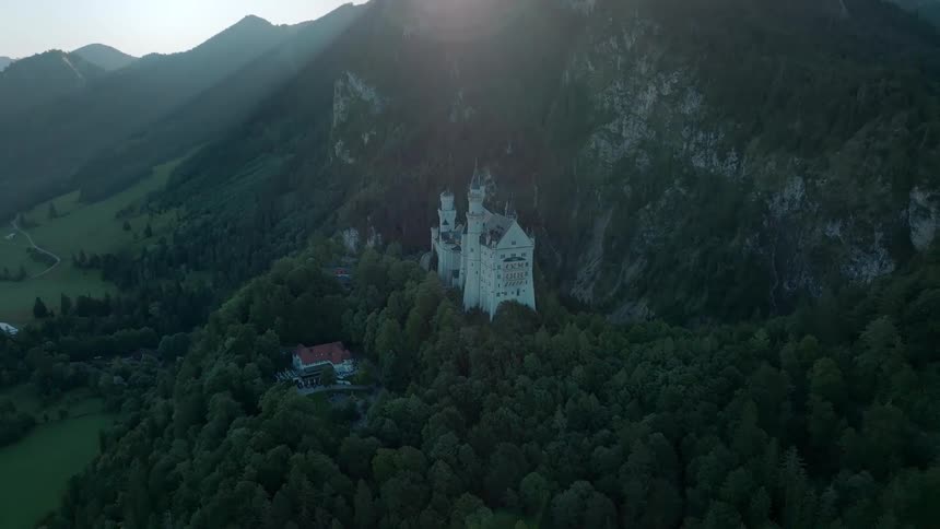 Castle stands on a forested hill in the shadow of a mountain on a sunny day