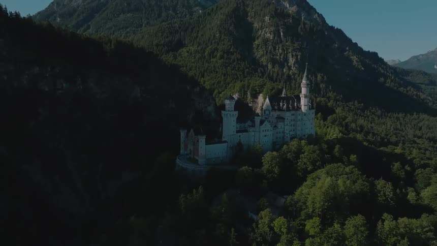Aerial view of neuschwanstein castle surrounded by lush forests and mountains