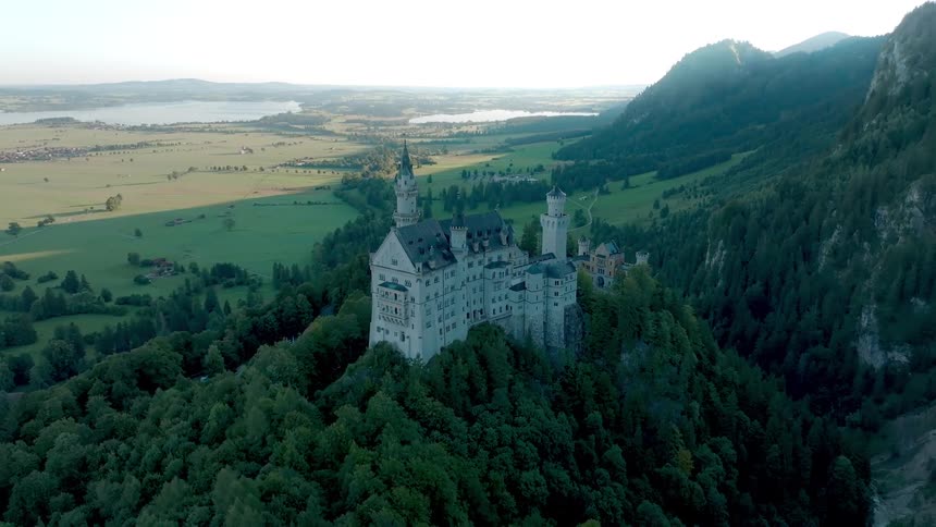Majestic castle rises atop a wooded hill surrounded by green valleys and mountains