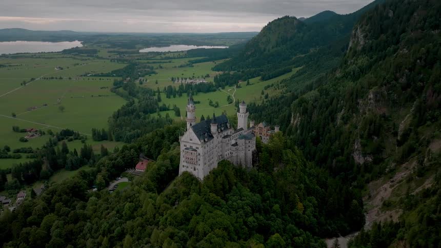 Aerial view of neuschwanstein castle on a wooded hill with mountains