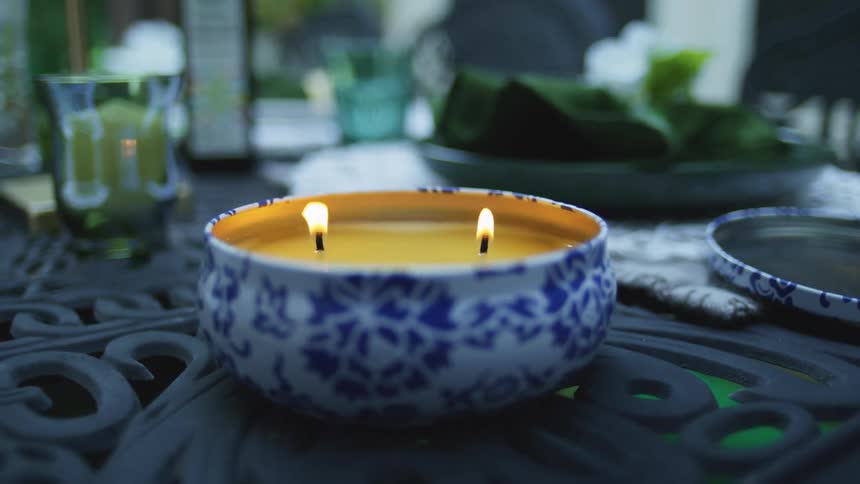 Lid to a bowl containing a candle with three wicks stands on an ironwork table
