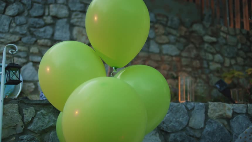 A cluster of lime green balloons floats in a stonewalled courtyard at dusk