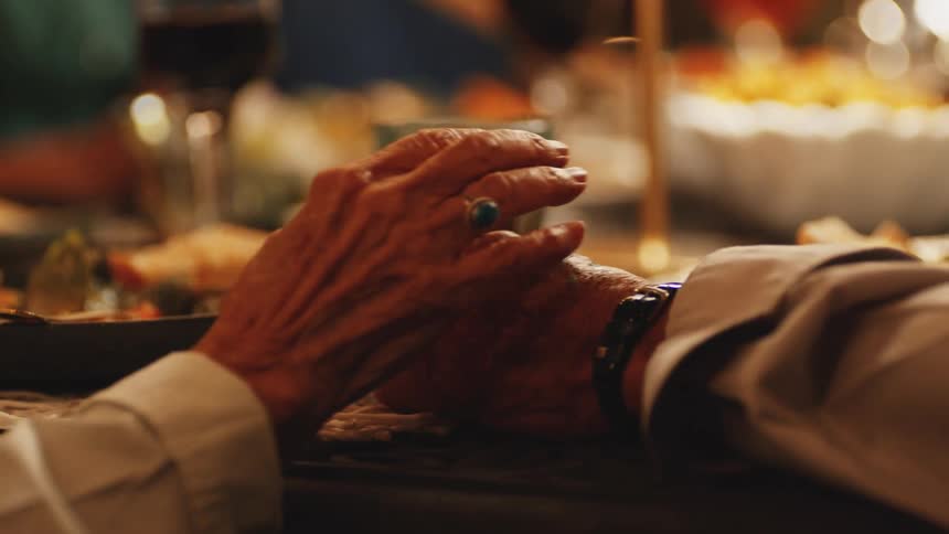Elderly man and woman take each others hands while sitting at the dinner table in the evening