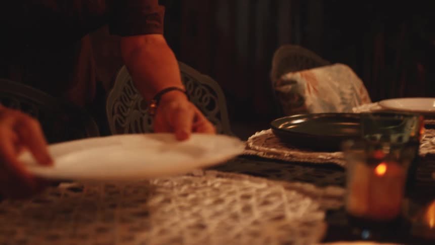 A woman sets a dark oval plates on a candlelit dining table