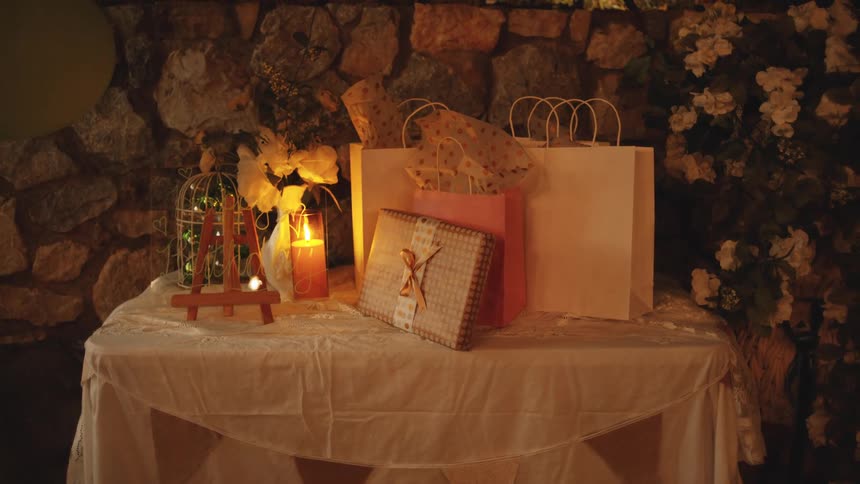 A table is filled with gift bags with a lit candle in a glass placed among them