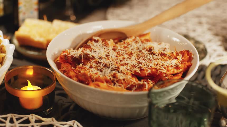 Artificial candle flickers next to a pasta dish on a wooden table