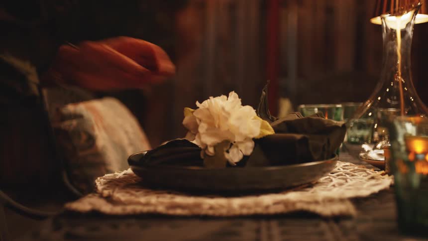 Hand adjusts a napkin on a dinner plate under warm lighting