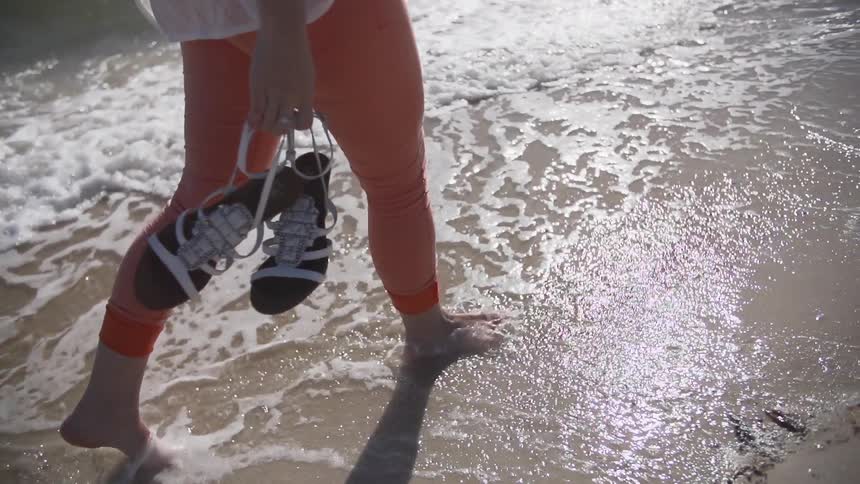 Woman holding sandals walking in the water