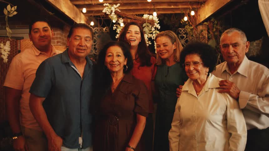A multi generational family smiles together under a warmly lit decorated pergola