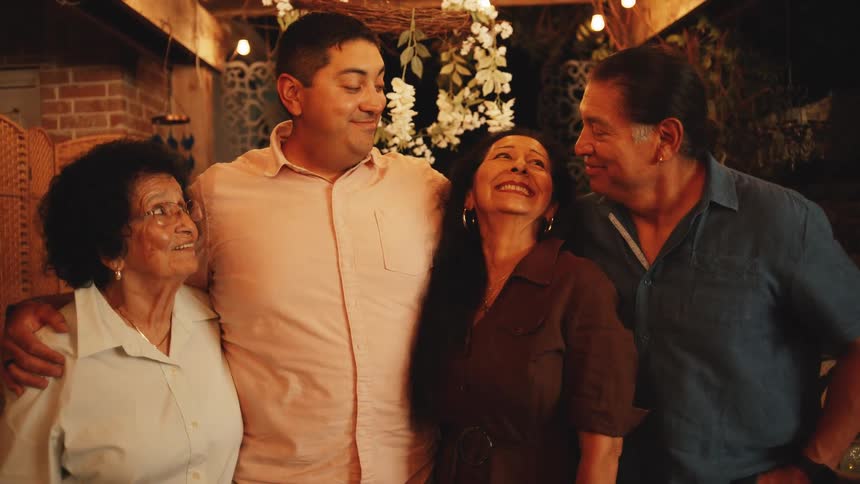 Hispanic young man with his parents and grandmother smiling and hugging during night time