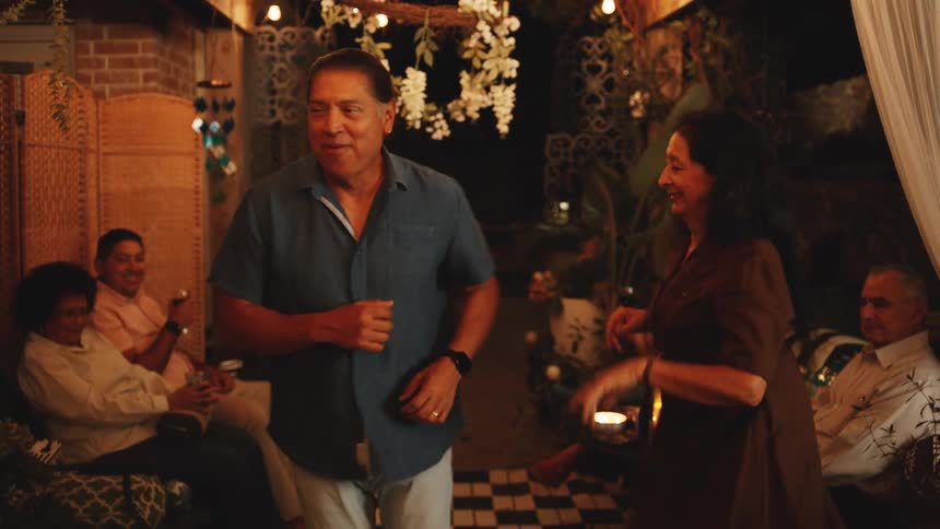 Couple joyfully dances under string lights around guests at a party