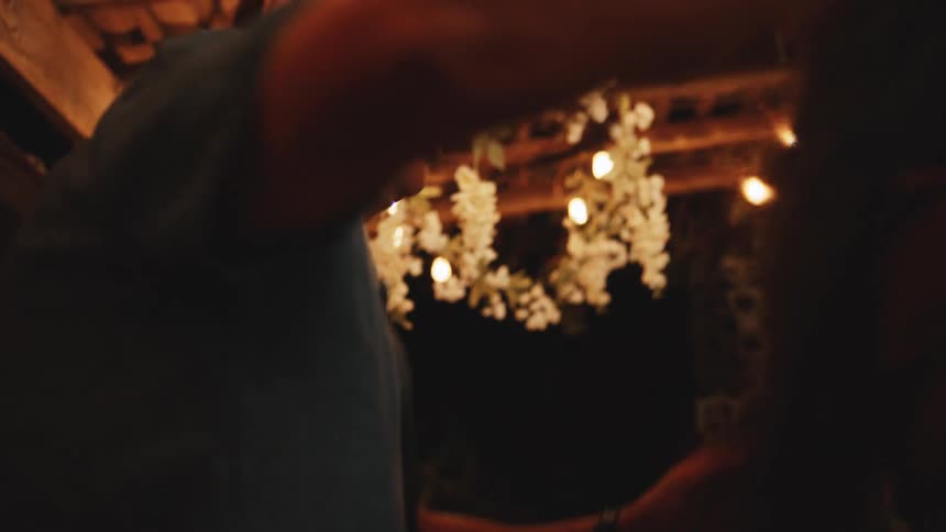 A man and a woman dance smiling at each other under string lights and wooden beams during a party