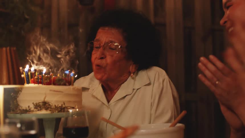 Elderly woman blowing out birthday candles at dinner table