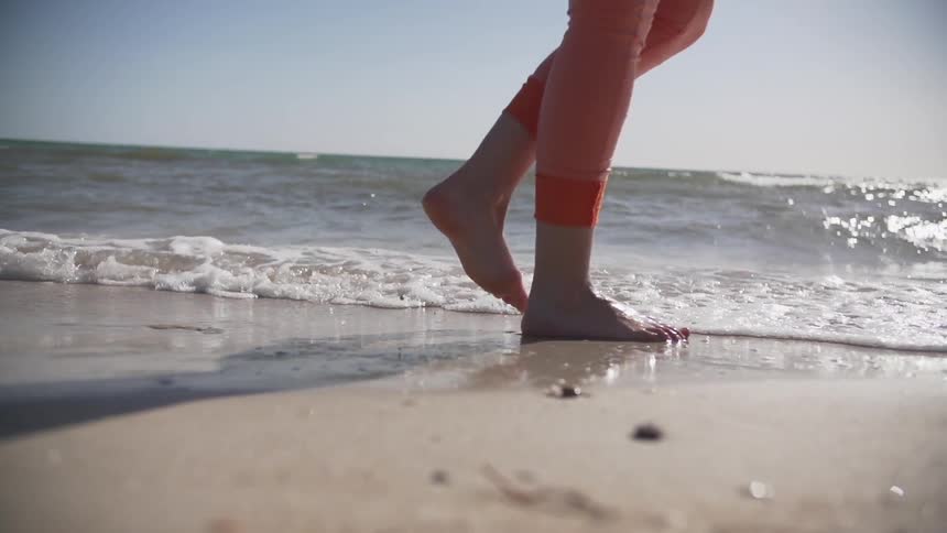 A person walks barefoot across the sand through the water