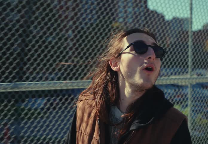 Man wearing sunglasses smiles outdoors near a metal fence