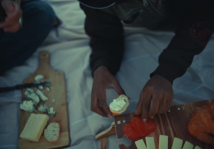 Group of friends having a picnic on the grass sharing cheese and bread at sunset