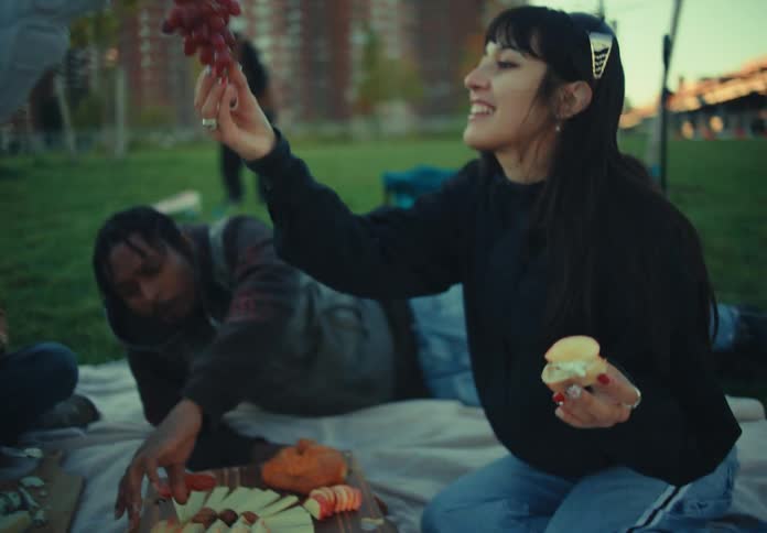 A group of friendsthree women and a young manenjoy a lively picnic on a grassy parkland at midday sharing fresh fruits and laughter under the bright sun