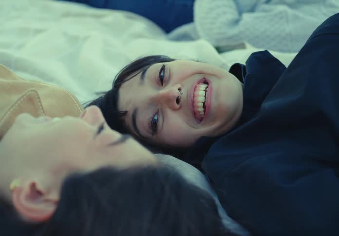Friends lying on a blanket smile while talking outdoors