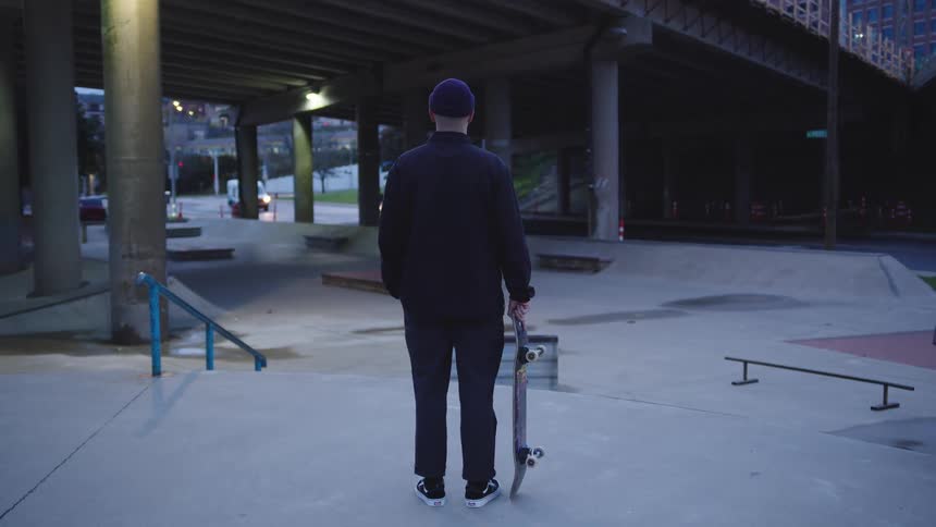Person standing with skateboard at skate park at dusk