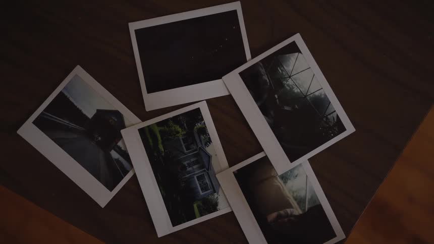 The video shows a closeup of several polaroidstyle instant film photos scattered across a dark wooden table the images on the prints depict various scenes including an outdoor house a roadcar and a dark night sky