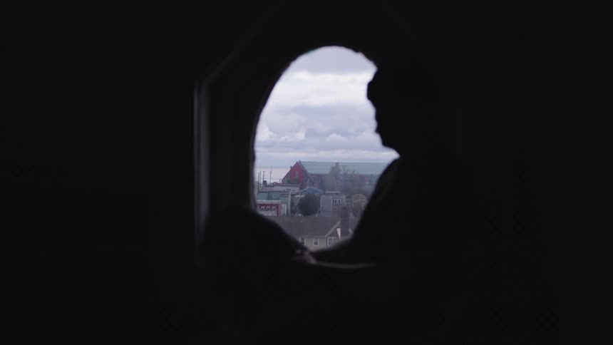 The man is sitting on the windowsill in the dark