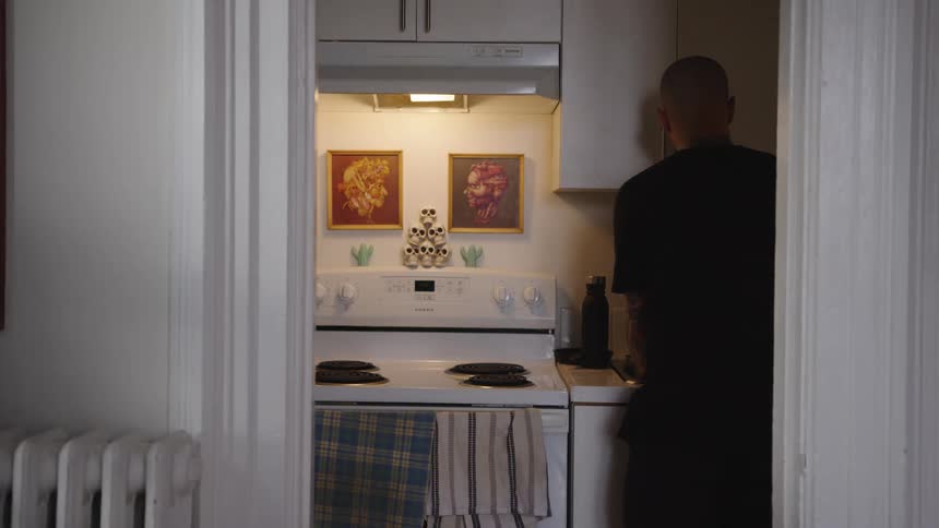 Man seen from behind prepares something in a lit kitchen