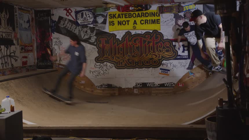 Skaters in action on an indoor ramp surrounded by posters graffiti and urban signage