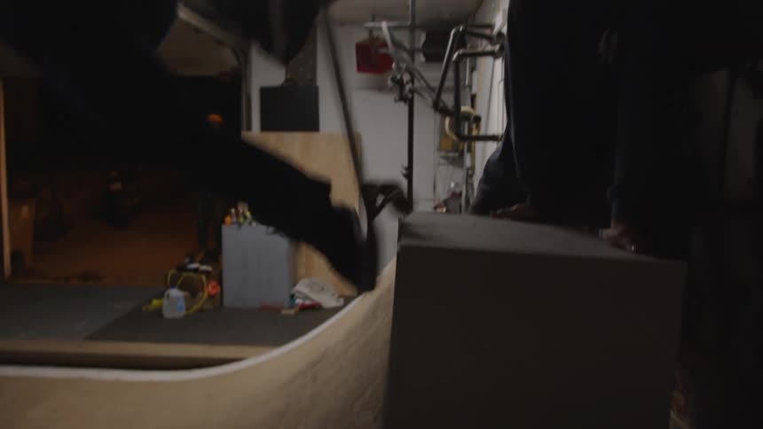 A man rides a skateboard back and forth on an indoor ramp attempting a trick midair he loses balance and tumbles off the board landing with a thud as the motion echoes through the space