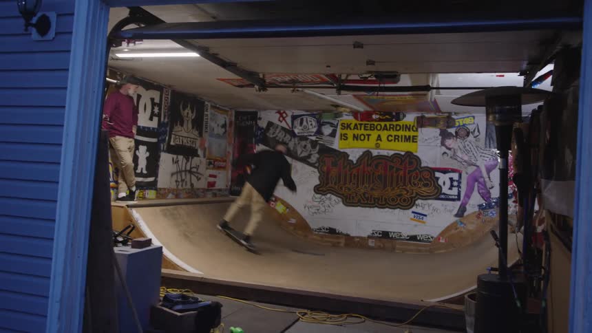 Two skateboarders practice tricks on a mini ramp decorated with posters and graffiti